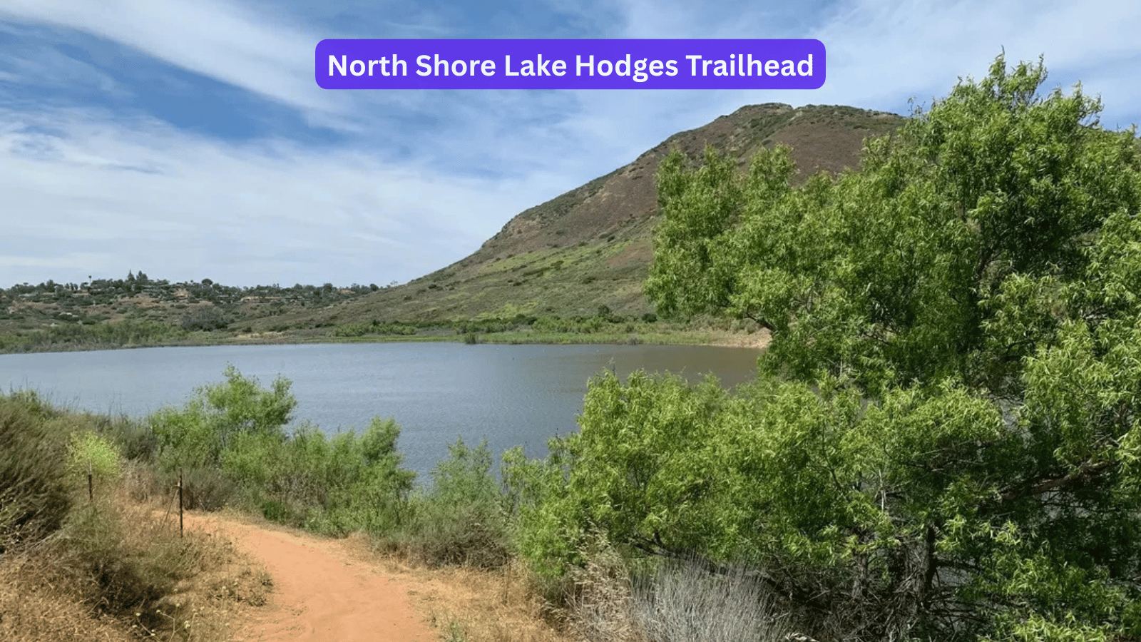 Dirt trail running down to the water at the North Shore Lake Hodges trailhead in Escondido, California, with a green ridgeline rising across the reservoir.