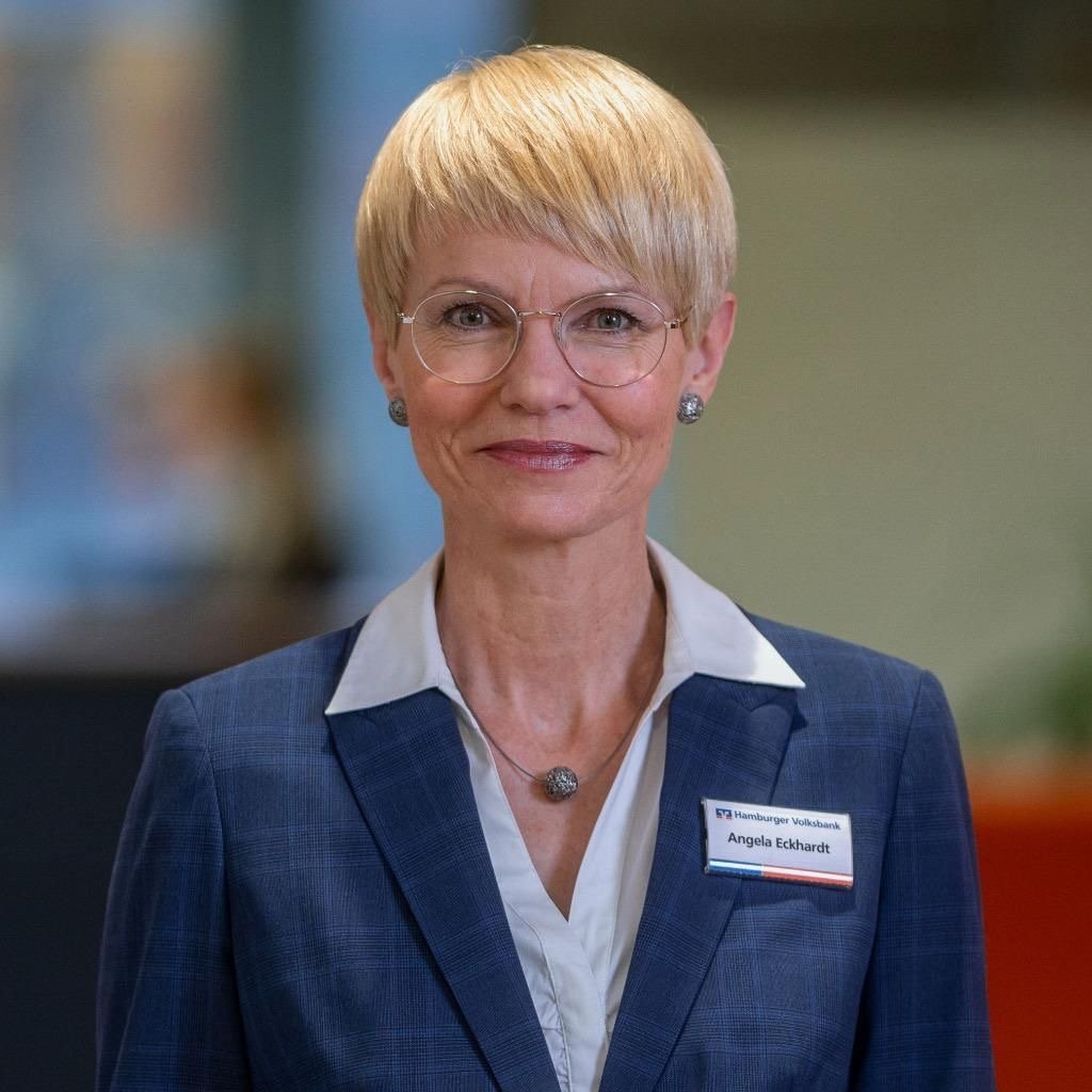 Woman with short blonde hair wearing glasses and business suit with name tag in office setting.