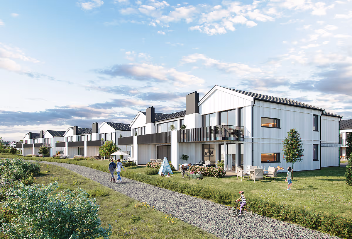 Row of modern white two-story houses with balconies along a gravel path and green lawns where people walk and bike.