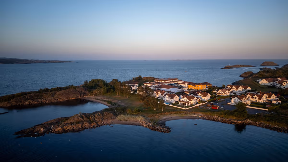 A coastal village with houses on rocky shores by calm blue sea under clear sky at sunset.