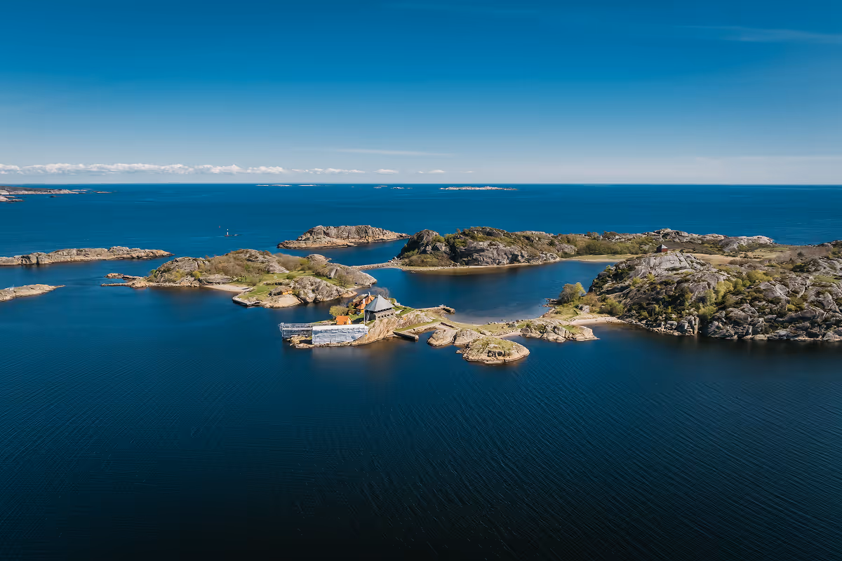 Aerial view of small rocky islands with sparse vegetation surrounded by deep blue sea under clear sky.