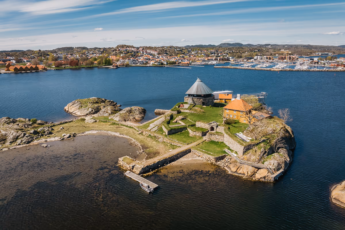 A small island with historic stone buildings and walls surrounded by blue water under a partly cloudy sky.
