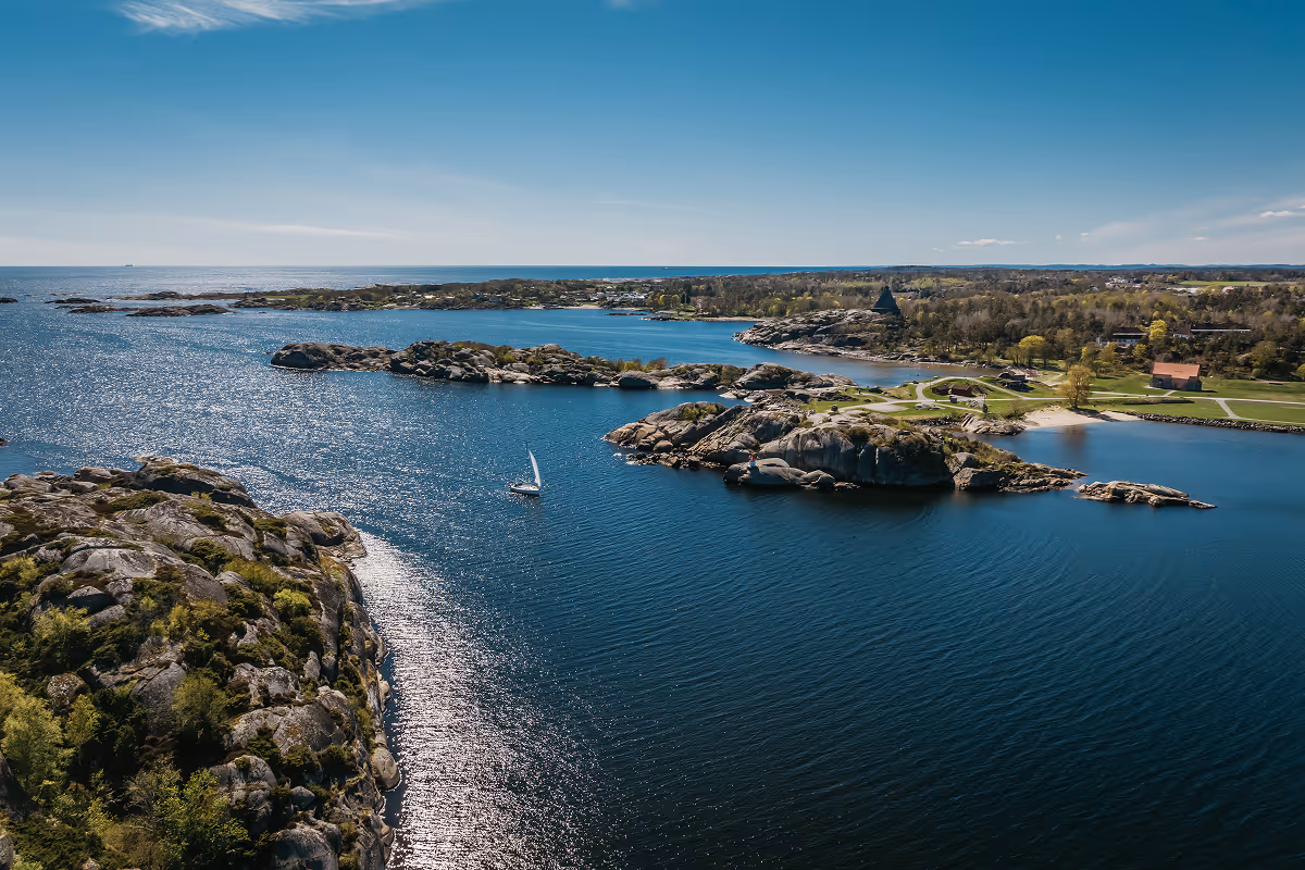 Sailboat on blue water near rocky islands with green trees under a clear sky.