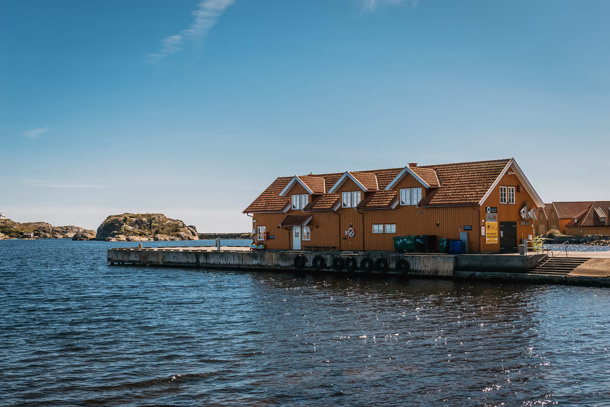 Orange wooden building with a tiled roof on a dock by calm blue water under clear sky.