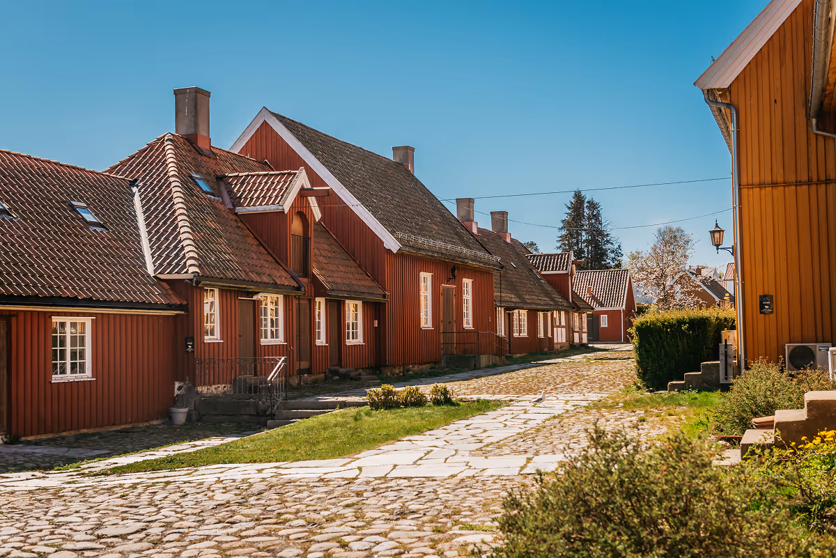 Cobblestone street lined with red wooden houses under clear blue sky.