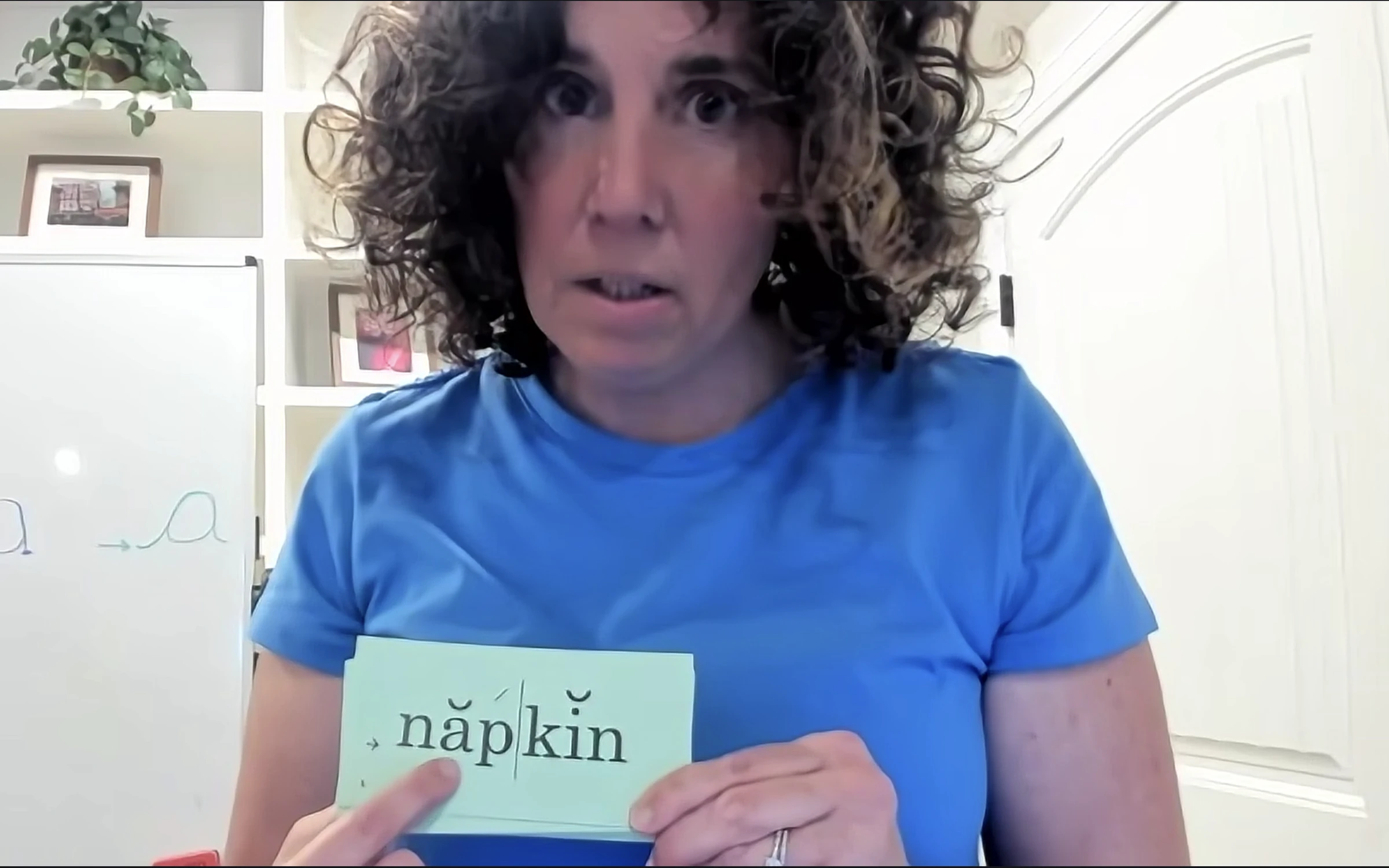 Elizabeth holding a syllable-division flashcard reading napkin during a virtual session