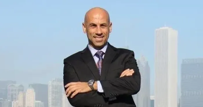 A man in a dark suit standing with his arms crossed in front of the Chicago skyline
