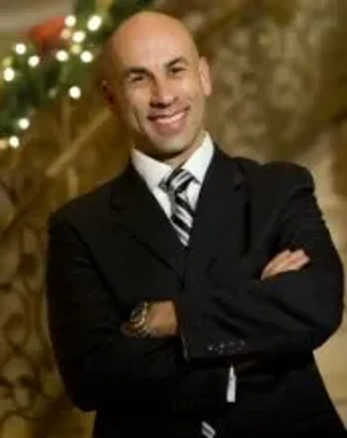 A man in a dark suit and striped tie standing with his arms crossed