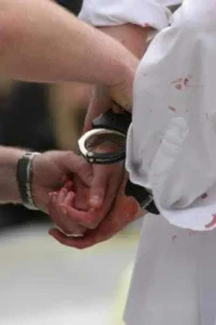 A police officer fastening handcuffs around the wrists of a person in a bloodstained white shirt
