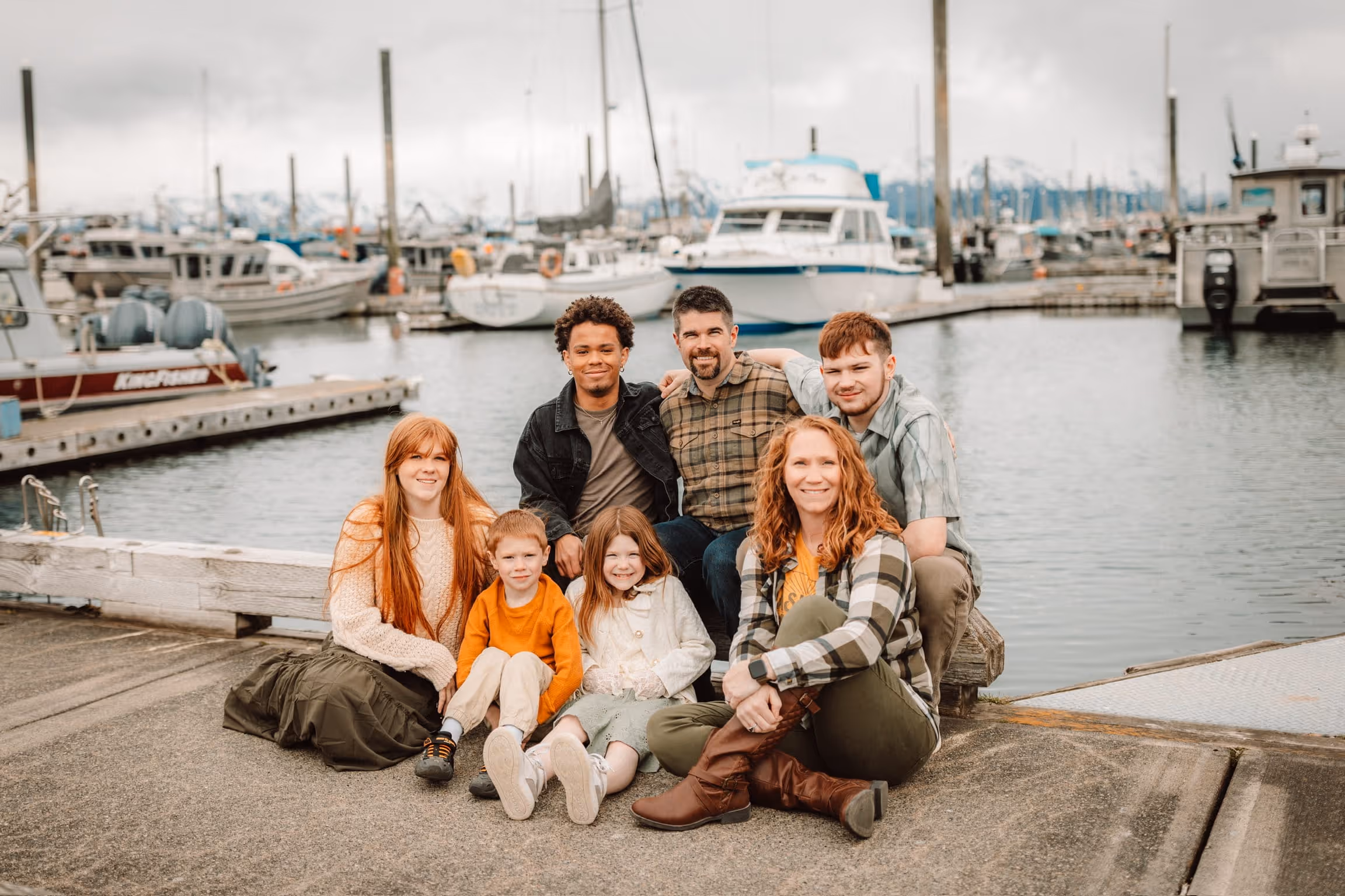 Seven people posing on a dock by marina with boats and water in the background.