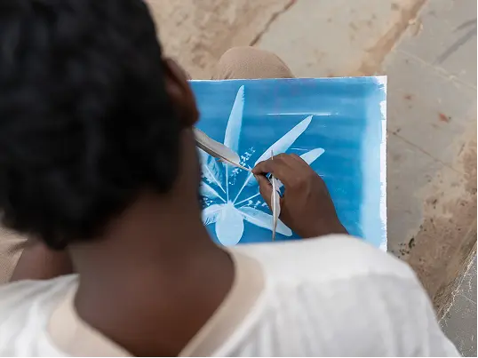 A person creates art on blue paper, using pigeon feathers as drawing tools in their hands