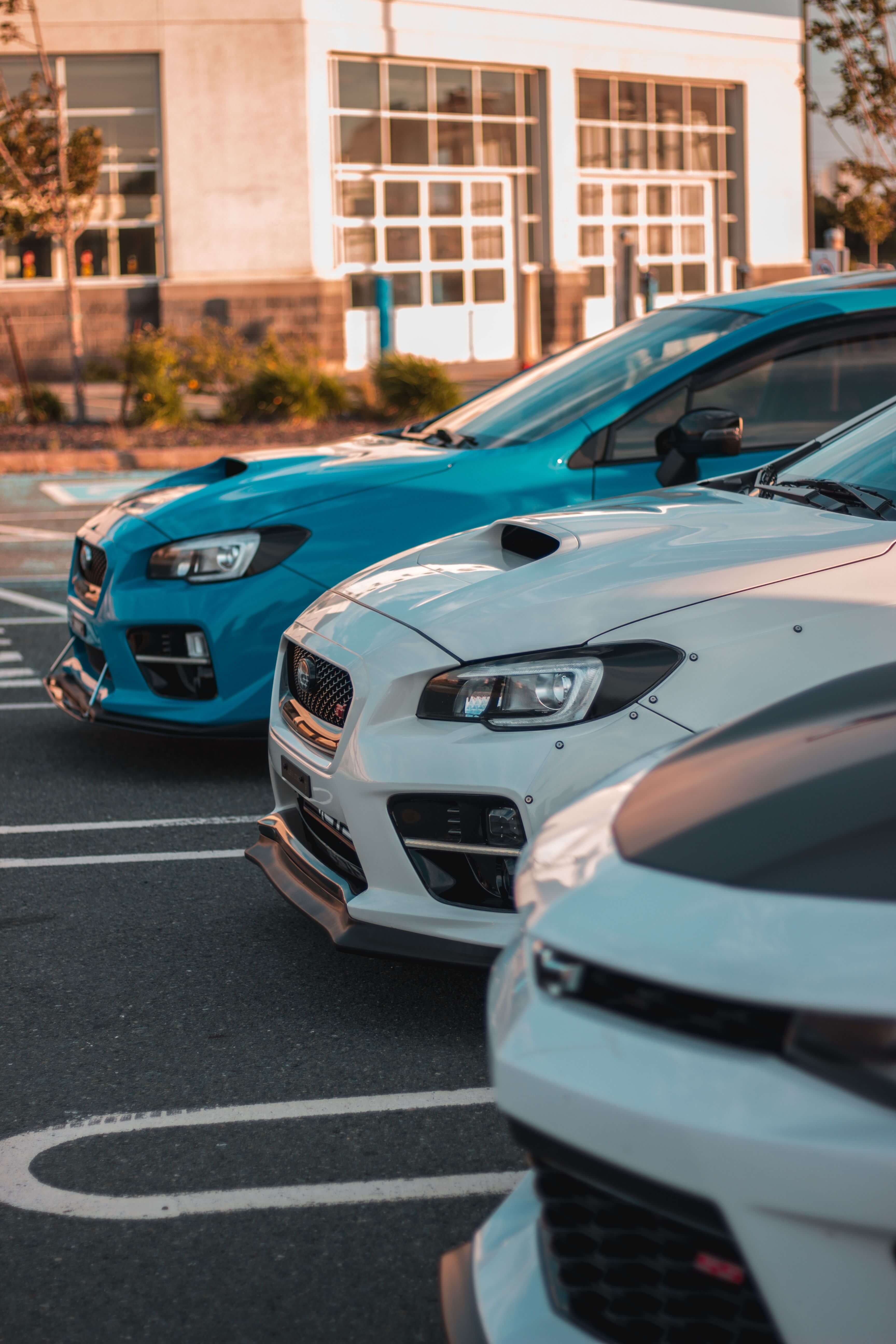 Front view of three parked sporty cars in a row in an outdoor parking lot near a building.