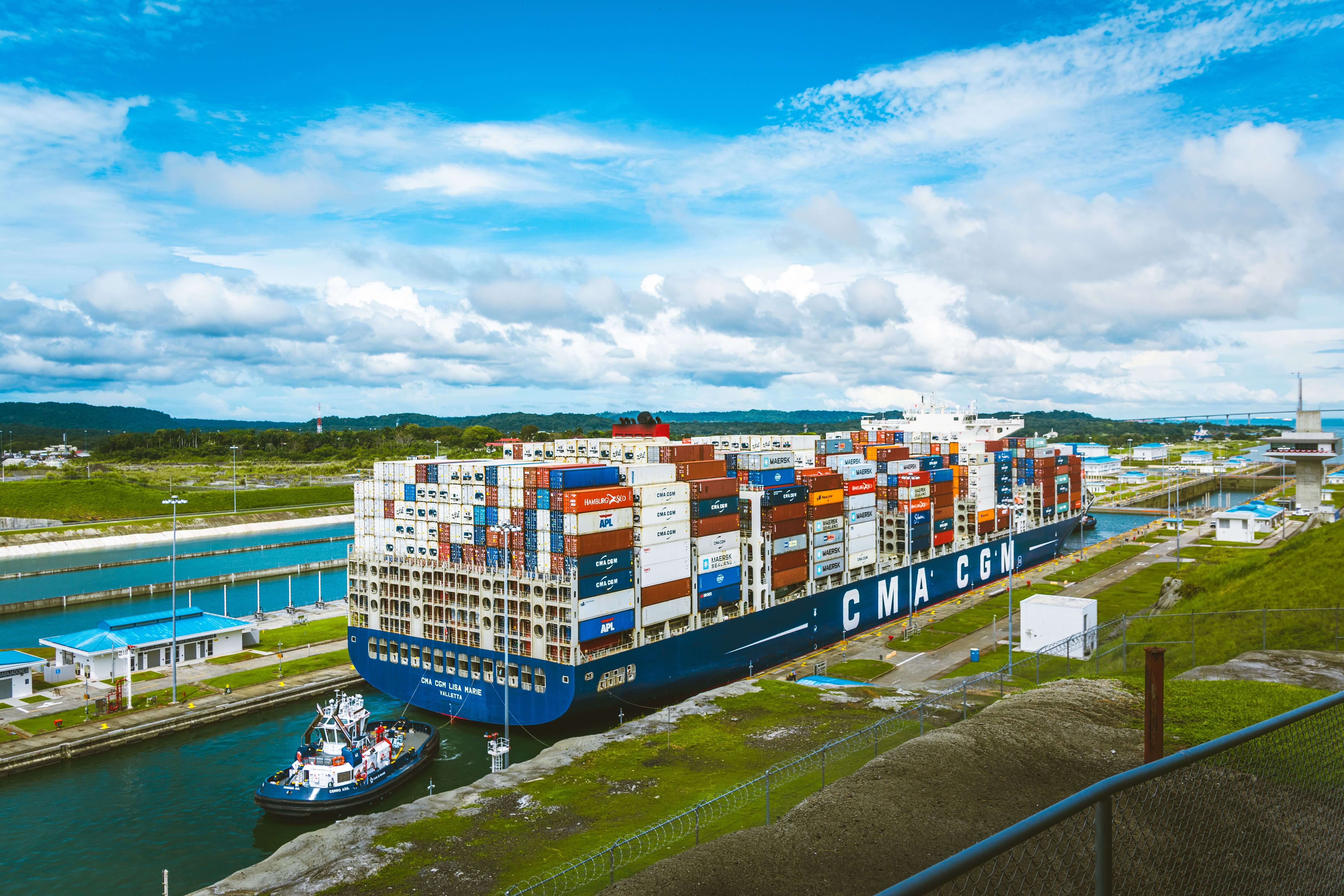Large container ship CMA CGM Lisa Marie passing through a canal lock with a tugboat assisting.