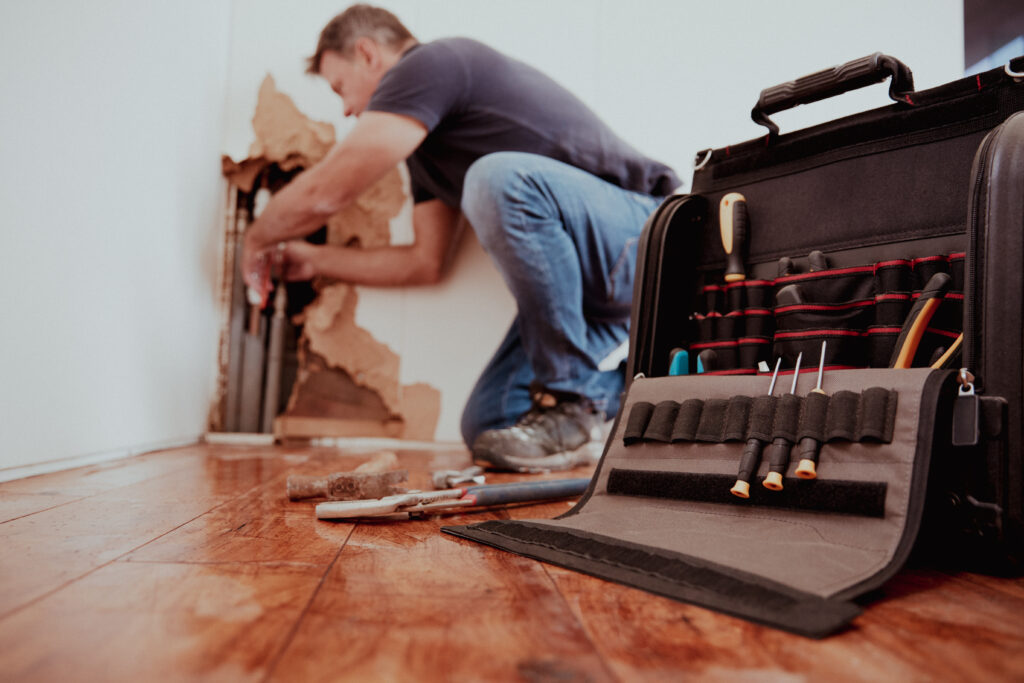 Man repairing a wooden floor with tools.
