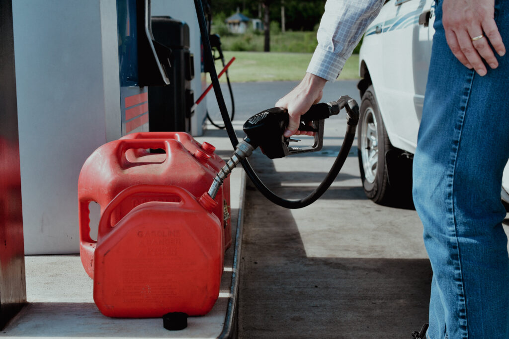 Person refueling a red gas container at a gas station.
