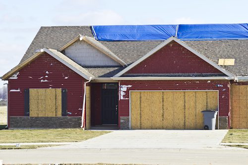red house with boarded windows and tapped roof
