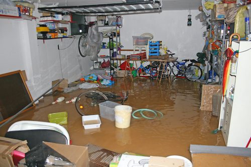 A cluttered room flooded with muddy water and various household items scattered around.