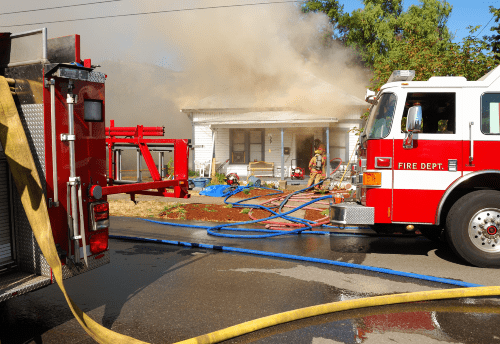 Firefighters battling a house fire with heavy smoke and fire trucks.