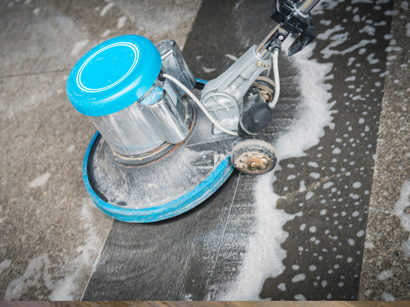 Close-up of a floor cleaning machine scrubbing a wet tiled surface with foam.