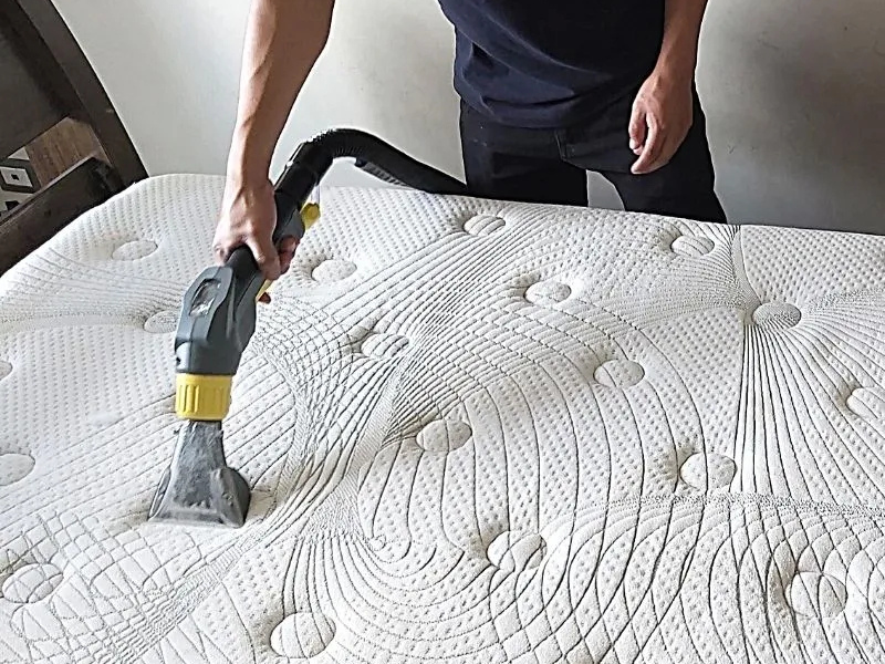 Person using a vacuum cleaner to clean a patterned mattress surface.