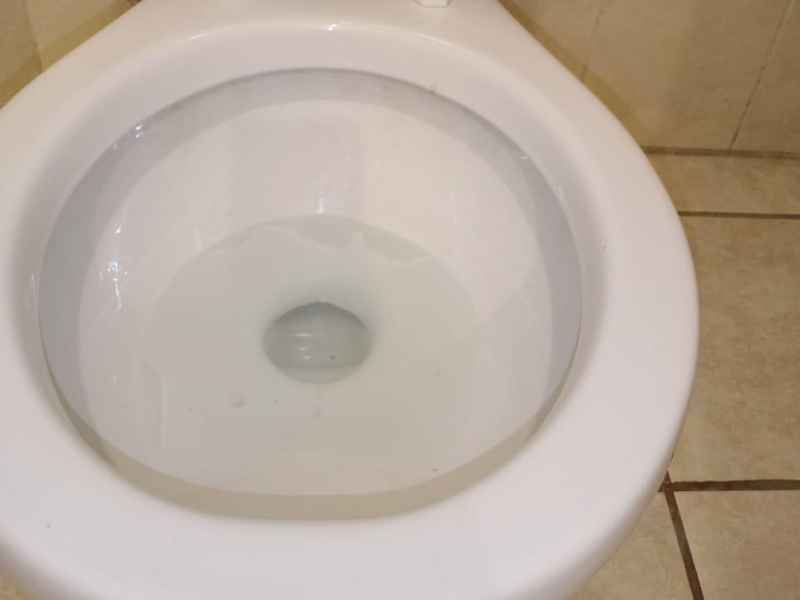 Top view of a clean white toilet bowl filled with clear water in a tiled bathroom.