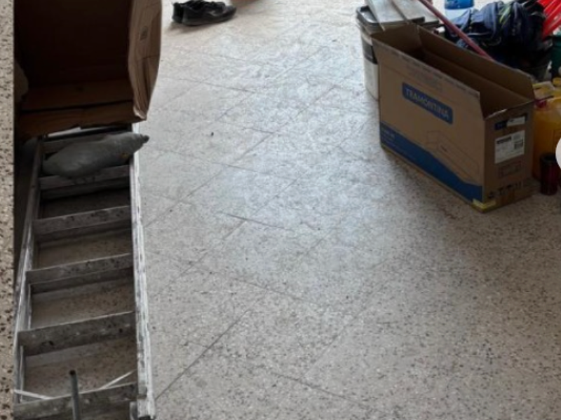 Indoor floor with scattered boxes, ladder, shoe, and cleaning tools in a cluttered space.