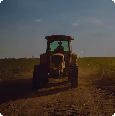 Silhouette of a person driving a tractor on a dirt road in a field at sunset.