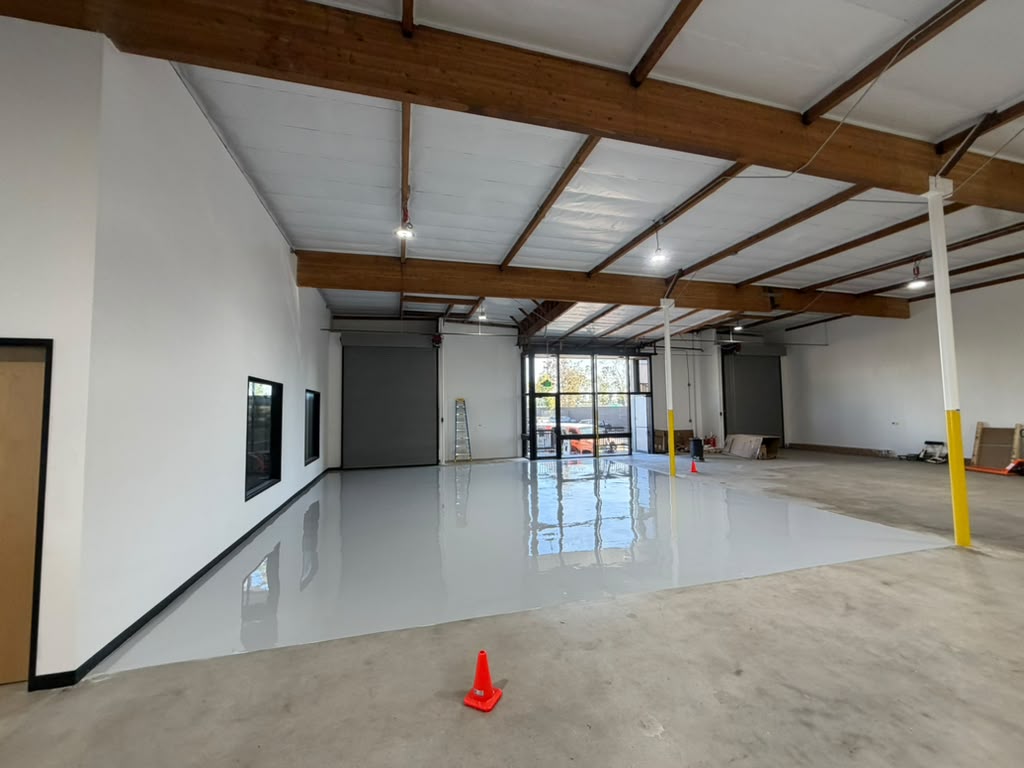 Light gray epoxy floor in a Los Angeles warehouse unit, with exposed timber beams and roll-up doors