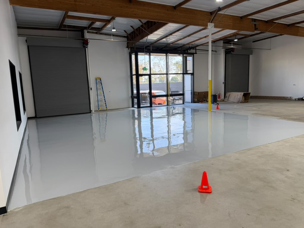 Finished high-gloss light gray epoxy warehouse floor reflecting the storefront glazing