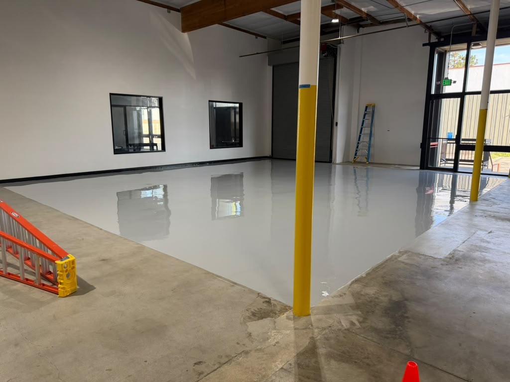 Freshly coated light gray epoxy floor beside the bare, ground concrete of the rest of the warehouse