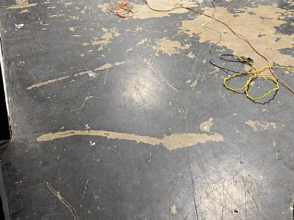 Worn black floor coating flaking off to bare concrete in the Los Angeles storage room before diamond grinding