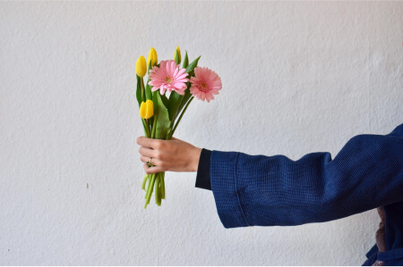Weiblicher Arm in blauer Jacke, der von rechts ins Foto ragt, so als werde er jemandem entgegengestreckt.Die Hand hält einen bunten Blumenstrauß