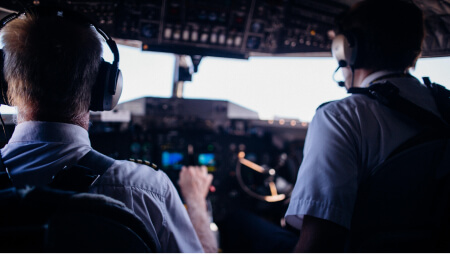 Piloten im Cockpit von hinten mit Headsets auf dem Kopf und Steuerungsarmaturen vor sich