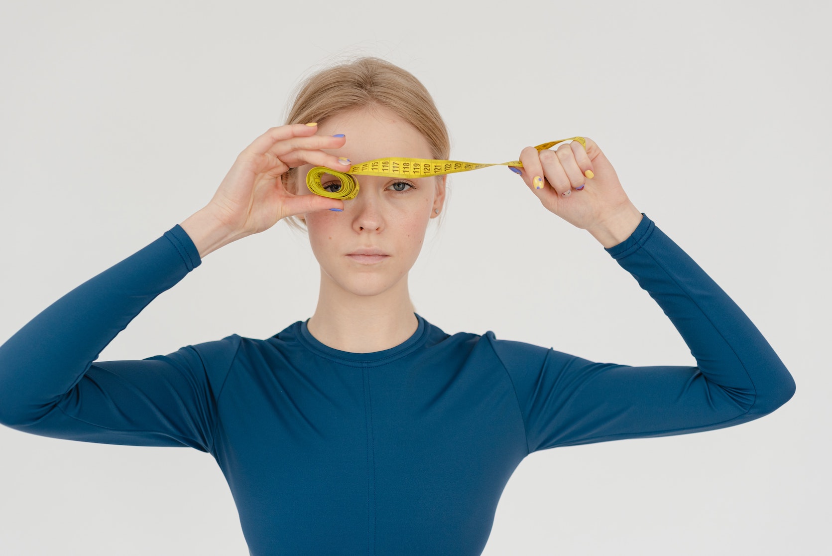Eine junge Frau hält sich ein Maßband vor die Augen