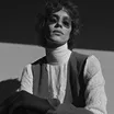 Black and white portrait of a person with curly hair wearing a turtleneck and jacket.