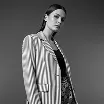 Black and white portrait of a young woman wearing a striped blazer and earrings against a plain background.