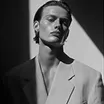 Black and white portrait of a serious young man wearing a blazer, lit by a strong shadow.
