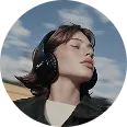 Young person with short hair wearing black headphones outdoors against a blue sky with clouds.