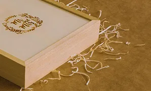 Stacked wooden books with gold embossed flower logo on cream cover and scattered paper shreds.