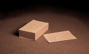 Stack of blank brown business cards with one card lying flat on a brown surface.