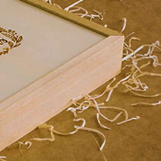 Corner of a wooden picture frame with white paper inside, surrounded by light wood shavings.
