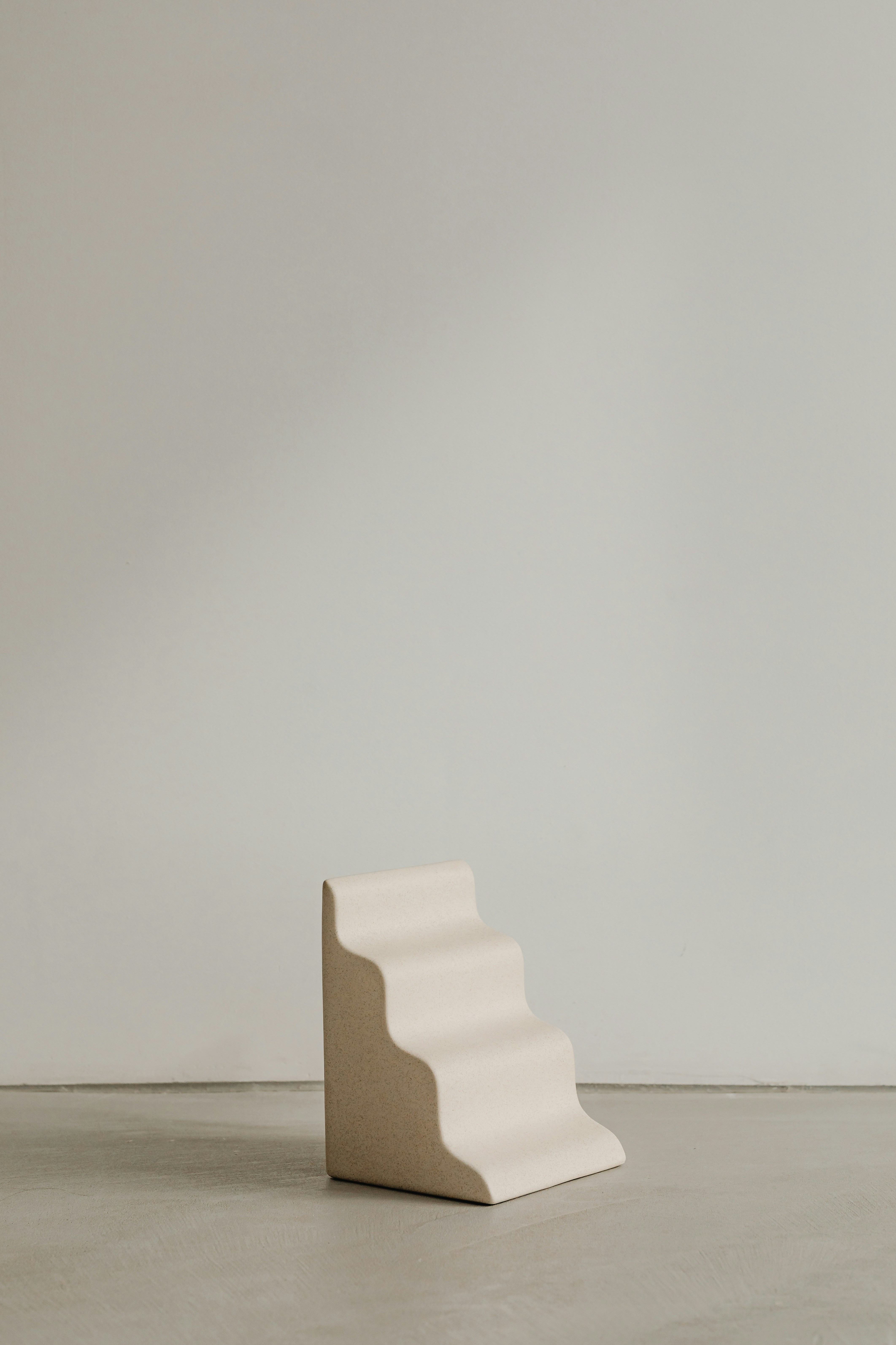 Small beige minimalist four-step sculpture or structure on a smooth floor against a plain wall.