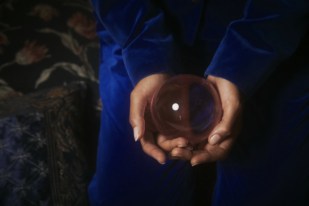 Person in blue velvet outfit holding a clear crystal ball with reflections in their hands.