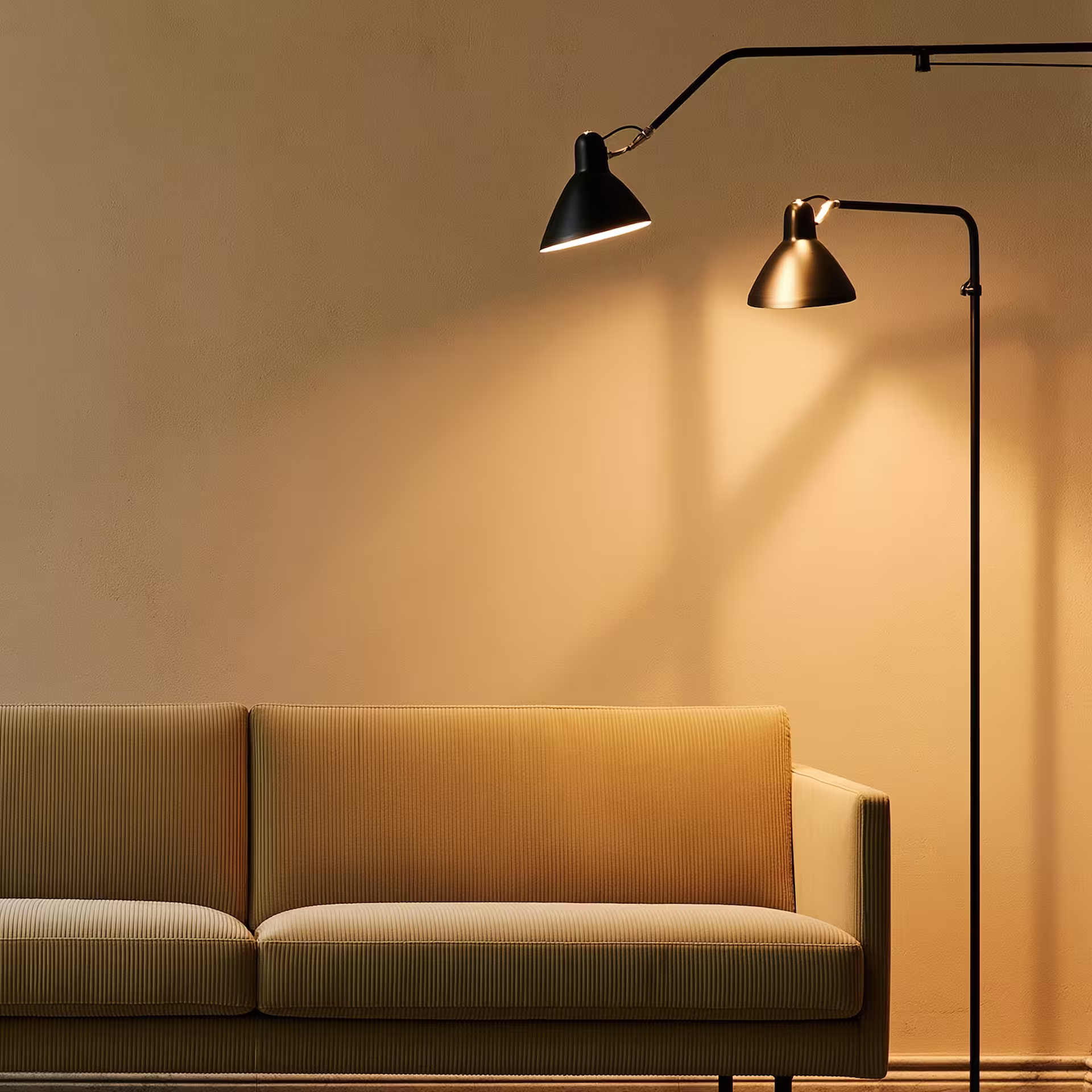 Modern beige sofa under two black floor lamps casting light on a plain beige wall.