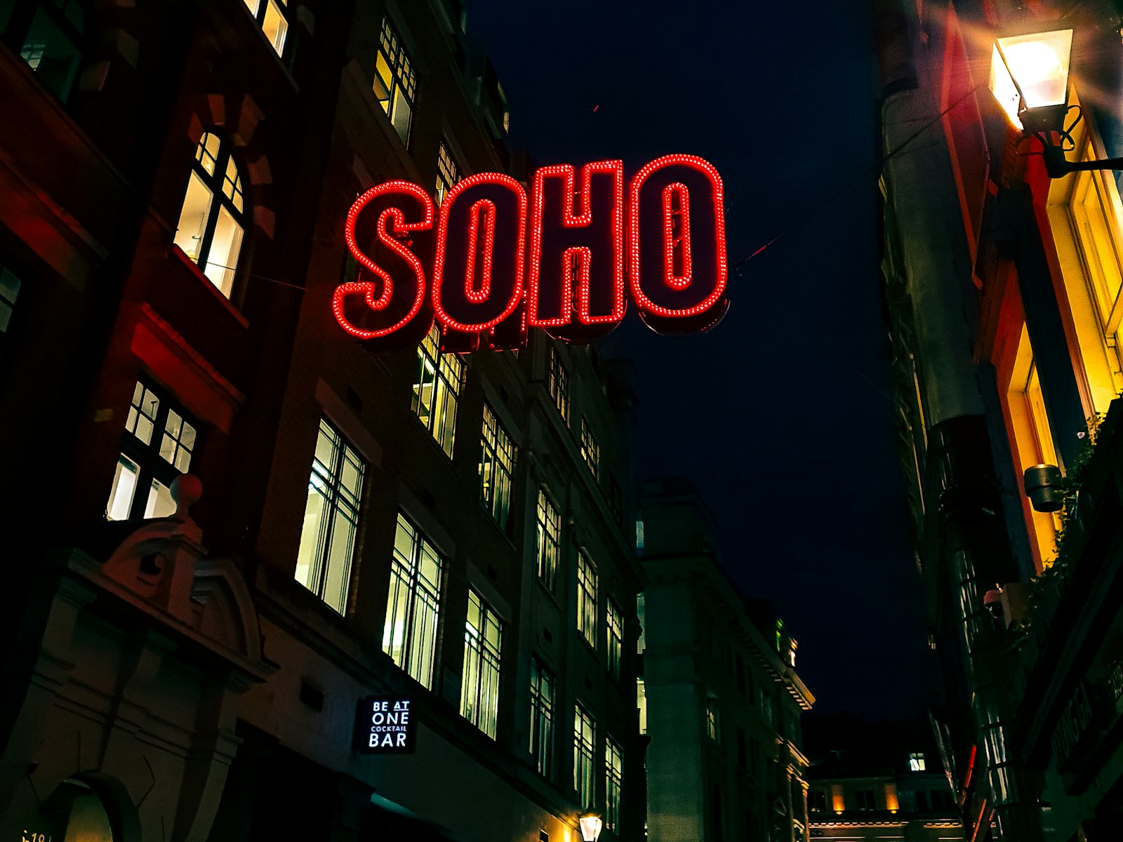 Red SOHO neon sign above a dark street in London at night