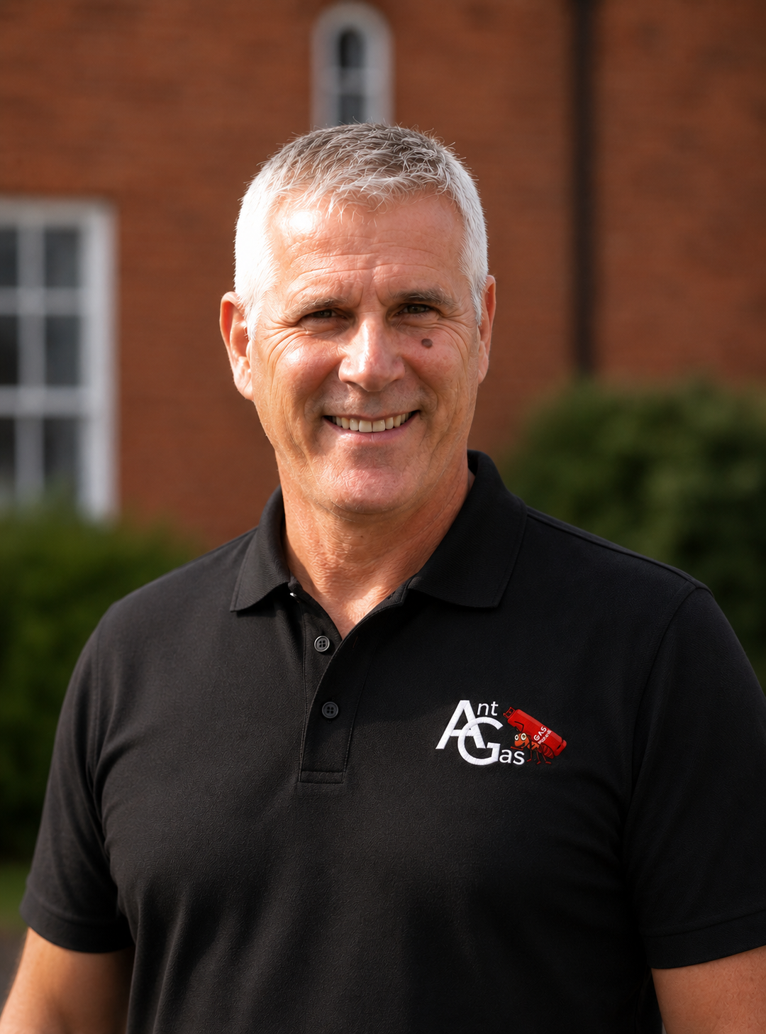 Smiling man with gray hair wearing black polo with Ant Gas logo on left chest outdoors.