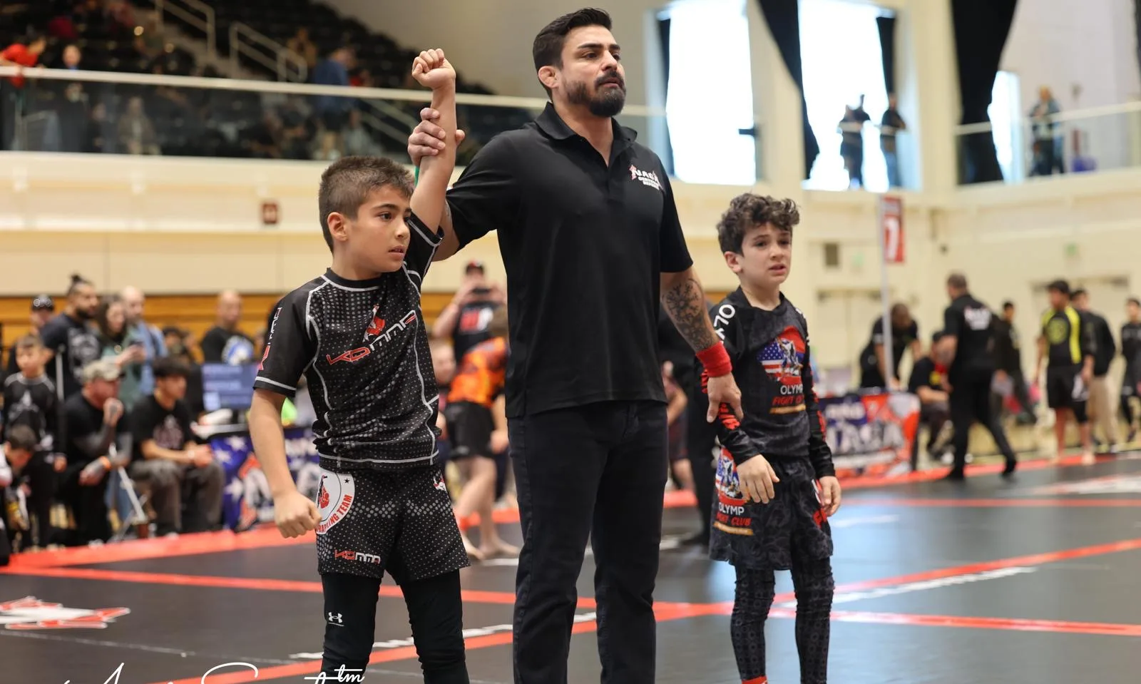 KD MMA coach raising a young athlete's hand in victory at a tournament