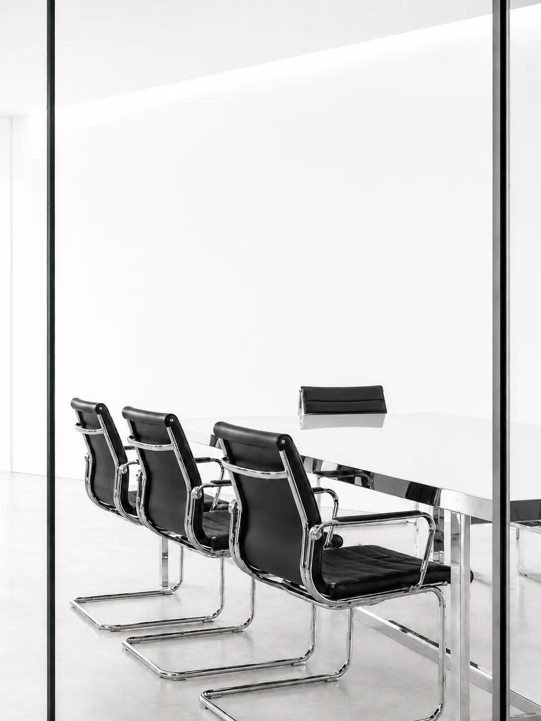 Drei schwarze Bürostühle mit Chromrahmen an einem weißen Besprechungstisch in einem modernen Raum.