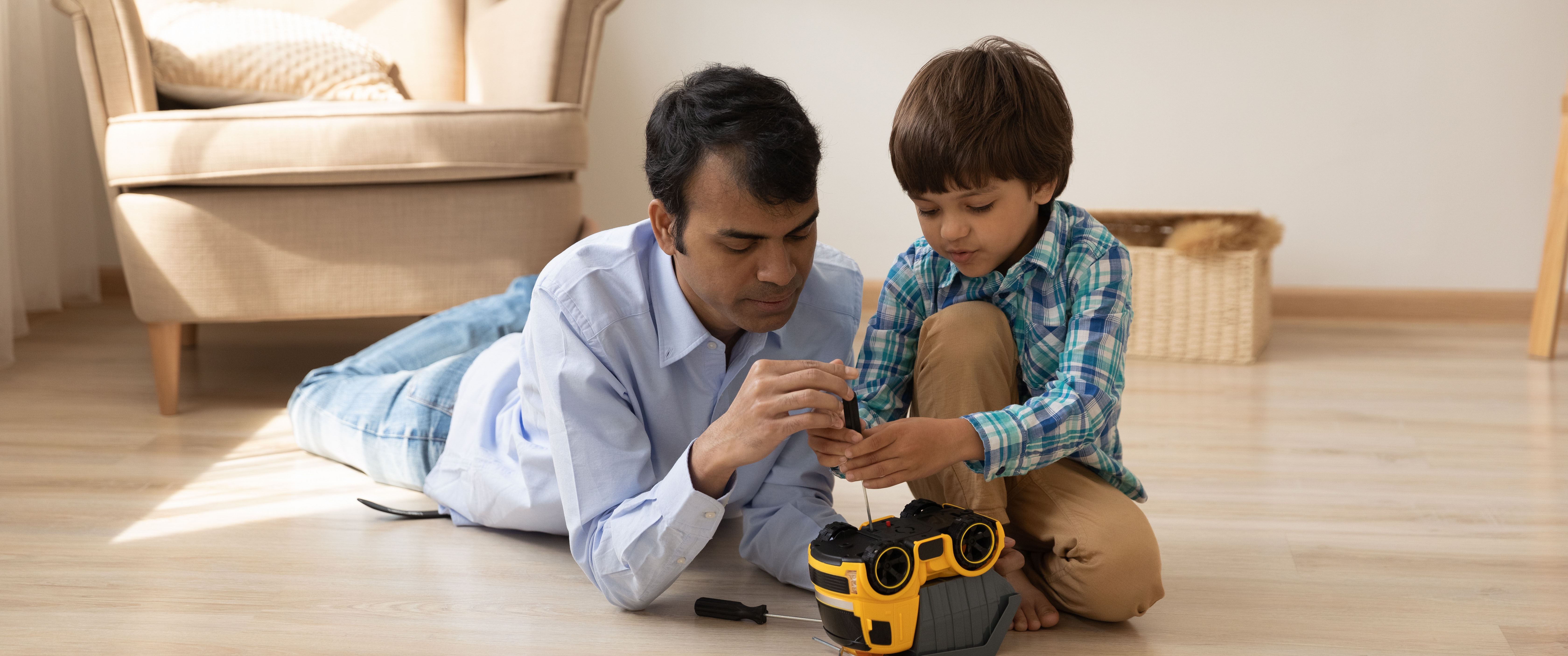 An adult lies on the floor beside a young child, both working on a toy together.