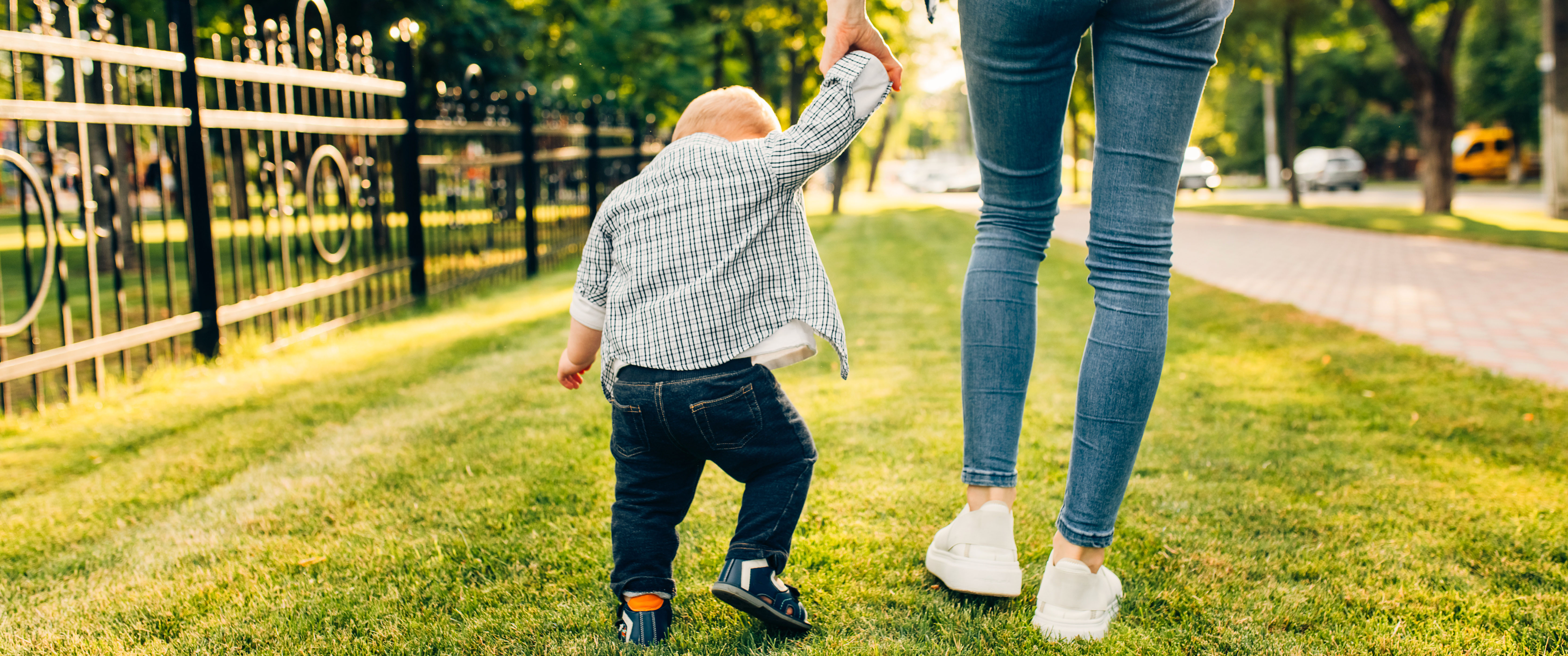An adult and a small child walk hand in hand across grass in low afternoon sun.